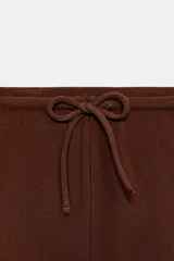 Pantalón palazzo de tiro medio en color marrón, confeccionado en tejido con textura. Cuenta con cintura elástica ajustable mediante cordones y diseño de pierna ancha.