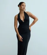 Vestido midi de color negro con escote halter y detalle metálico en el busto. Presenta fruncidos laterales que realzan la silueta y un diseño elegante y ajustado.