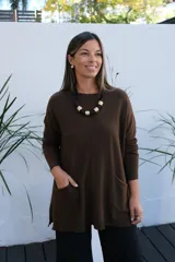 Sweater de tejido de punto en color chocolate, con corte holgado, cuello redondo y mangas largas. Presenta un diseño con bolsillos frontales integrados y terminaciones acanaladas en puños y ruedo.