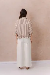 Camisa de rayas verticales blancas y marrones, de calce relajado y largo corto con volado en el ruedo. Presenta cuello camisero clásico, mangas tres cuartos con puños amplios, abotonadura frontal y un bolsillo aplicado en el frente.