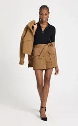 Remera de punto acanalado color negro, con silueta ajustada, cuello polo estructurado, mangas cortas y cierre frontal con cremallera metálica y colgante decorativo.