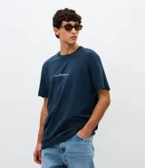 Remera de algodón azul marino con cuello redondo y mangas cortas. Presenta un diseño con estampa minimalista en el frente y una gran ilustración artística del skyline de Nueva York con la frase 'Connected by Movement' en la espalda.