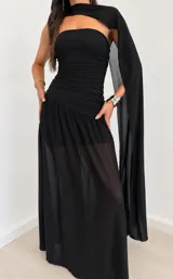 Vestido largo negro de diseño elegante, con cuerpo drapeado estilo strapless, falda larga con capa exterior transparente y estola o bufanda integrada al cuello.
