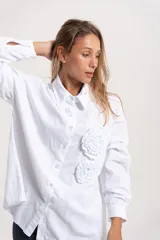 Camisa de pana blanca con cuello clásico, cierre frontal de botones y aplicaciones florales en relieve en el frente.