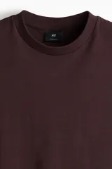 Remera de punto de algodón pesado color marrón oscuro (bordó/ciruela), con cuello redondo ribeteado, hombros caídos y corte oversized.