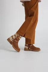 Bota estilo biker de caña media, confeccionada en cuero negro con detalles en gamuza marrón. Presenta correas ajustables con hebillas metálicas, tachas decorativas y suela track dentada.