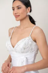 Vestido largo de novia blanco con corte imperio y tirantes finos. Presenta el cuerpo superior bordado a mano con abalorios y pedrería, faja drapeada con lazo lateral y falda fluida con cola.