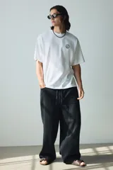 Remera blanca de punto de algodón de peso medio, con cuello redondo ribeteado y hombros caídos. Presenta un pequeño estampado minimalista de un emoji con la boca recta en el pecho.