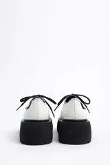 Zapato blucher acordonado de piel color blanco con ojetes metálicos y etiqueta textil personalizada en el lateral. Plataforma de goma logotipada color negro.