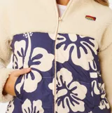 Campera tipo puffer de Rip Curl, con diseño combinado de corderito color beige en la parte superior y mangas, y panel frontal acolchado en color azul marino con estampado floral. Cuenta con cierre frontal completo y cuello alto.