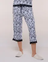 Conjunto pijama de pantalón capri y remera René Rofé, de color blanco con estampado floral en tonos azules y celestes. Remera de manga corta con escote en V y detalles de encaje azul en el escote, las mangas y el ruedo. Pantalón capri con cintura elastizada, cordón de ajuste y encaje en el ruedo.