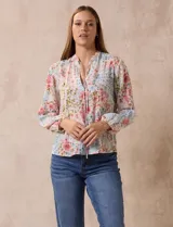 Blusa de gasa plisada con estampado floral en tonos rosas y celestes. Presenta cuello a la base con escote en V y lazo de ajuste frontal, mangas largas con puños elásticos y corte recto.