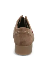 Zapato tipo wallabee de Hush Puppies, confeccionado en cuero gamuzado color marrón. Presenta costuras a la vista en tono claro, cordones al tono y suela de goma texturizada. Incluye etiqueta lateral con la marca y bandera británica.
