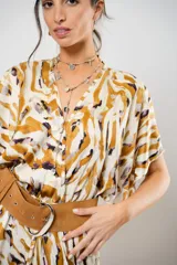 Vestido largo con estampado animal print en tonos camel, blanco y negro. Tiene escote en V, mangas cortas tipo murciélago y tajo frontal. Incluye cinturón ancho de cuero color camel.