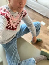 Sweater de punto grueso color gris claro con cuello redondo y diseño con motivos geométricos en tonos rosa y borgoña en la parte superior del pecho y hombros.