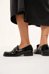 Mocasines negros de charol arrugado con horma redondeada y detalle de presilla con hebilla y ojalillos.