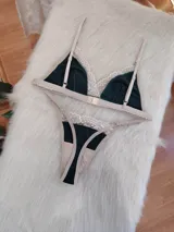 Conjunto de lencería compuesto por bralette triangular y tanga, confeccionado en algodón color verde inglés con detalles de encaje en tono nude. El bralette cuenta con breteles ajustables y broche regulable, mientras que la tanga presenta laterales ajustables.