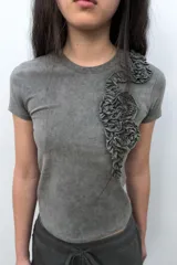 Camiseta de algodón con efecto lavado, cuello redondo y manga corta. Presenta un detalle decorativo de flores en relieve confeccionadas en el mismo tejido sobre el lado izquierdo del pecho.