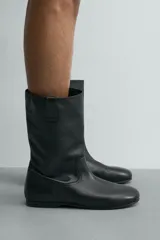 Bota de caña media fabricada en piel lisa, con diseño minimalista, tiradores laterales y suela a tono con ligero tacón.