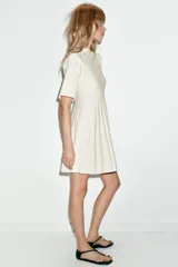 Vestido corto de punto rib color crema, con cuello redondo, manga corta abullonada y falda plisada.