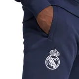 Pantalón de jogging azul marino, corte regular, con cintura elástica y cordón regulable. Presenta el escudo del Real Madrid bordado en la pierna izquierda y el logo de Adidas en la pierna derecha.