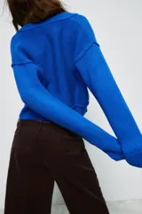 Jersey de punto color azul eléctrico con escote en pico, manga larga y detalle de costuras marcadas en los hombros. Presenta un corte ligeramente cropped con puños y ruedo acanalados.