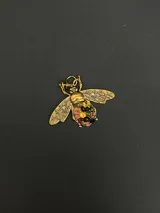 Dije con forma de abeja en metal dorado con alas texturizadas y cuerpo decorado con pequeñas piedras naturales multicolor.