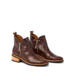 Botas cortas de cuero vacuno color marrón, con diseño de caña baja y cierre metálico en ambos laterales. Presentan un taco cuadrado de madera y suela de goma.