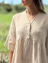 Vestido corto de lino color beige claro, con cuello mao, escote con botones de nácar, mangas tres cuartos con volados y ruedo con volado.