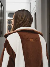 Campera con capucha, de tela tipo peluche a rayas verticales color marrón y blanco, con ribete color beige.