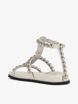 Sandalias planas color blanco con tiras decoradas con tachas plateadas y cierre de velcro.