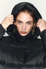 Plumífero corto acolchado color negro, resistente al agua y al viento. Cuenta con cuello subido, capucha extraíble, cierre frontal con cremallera y botones magnéticos, mangas largas con puños elásticos y bajo ajustable con stoppers.