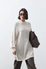 Vestido corto de punto en color beige, con cuello alto acanalado, mangas largas con puños ajustados y diseño holgado.