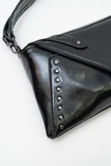 Bolso de mano tipo sobre color negro, confeccionado en cuero sintético, con solapa frontal decorada con tachas metálicas y correa larga ajustable y extraíble.
