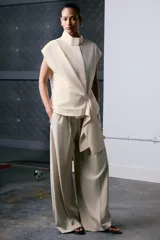 Camisa sin mangas confeccionada en algodón, con cuello subido y diseño cruzado con detalle de fajín asimétrico lateral. Cierre frontal con botones ocultos.