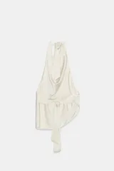 Top satinado color crema con cuello halter y lazada en la parte trasera. Presenta un escote drapeado asimétrico.