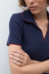 Remera de punto tipo polo color azul marino, con cuello abierto y detalles de vivo en color rojo en el borde del cuello y las mangas.