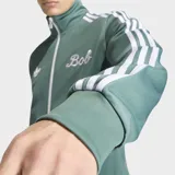 Campera deportiva Adidas Originals, modelo colaboración Bob Marley, color verde con las icónicas tres tiras blancas en las mangas. Presenta cuello alto, cierre frontal con cremallera y logo del Trifolio bordado en el pecho.