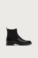 Bota estilo Chelsea de color negro, con parte superior lisa, paneles elásticos laterales y tirador trasero. Cuenta con horma redonda y suela con ligero tacón.