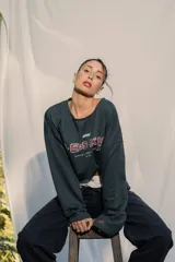 Crewneck (jersey de cuello redondo) unisex color gris oscuro, con estampado frontal que dice "RE:SKIN" y texto pequeño debajo. Presenta mangas largas y corte holgado.