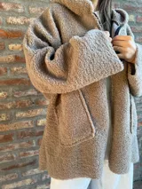 Campera de corderito color verde oscuro, con diseño holgado, cuello alto y manga larga. Presenta una etiqueta de cuero sintético en la manga.