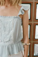 Top celeste con escote recto, tirantes con volantes y bordado floral en el centro.