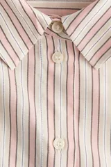 Camisa de corte oversize, con diseño de rayas verticales en tonos rosados, blancos y beiges, cuello clásico, mangas largas con puños abotonados y cierre frontal de botones.