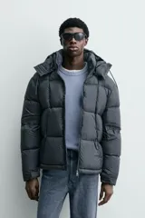 Cazadora acolchada tipo puffer de corte regular, confeccionada en tejido técnico repelente al agua. Cuenta con cuello subido, capucha ajustable y desmontable, cierre frontal con cremallera, bolsillos laterales con cremallera oculta y puños ajustables con tira adherente.