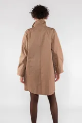 Gabardina color beige de largo medio con corte regular, fabricada en nailon repelente al agua. Tiene costuras interiores con ribete de nailon, cierre frontal con botones ocultos, escote medio bajo con cuello solapa, puño ancho con ventilación, manga de una pieza con costura en el puño, bolsillo de ribete inclinado y parche de logotipo de silicona.