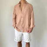 Camisa de lino con corte oversize, cuello clásico y cierre frontal con botones. Presenta mangas largas con puños arremangados y una textura rústica característica del tejido.