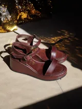 Sandalias de plataforma con taco cuña color marrón y tiras doradas metalizadas en el empeine y el talón. Cuentan con tira ajustable con hebilla metálica en el tobillo.