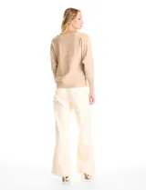 Buzo de tejido fino color beige, con mangas tipo dolman y puños ajustados. Presenta un diseño frontal decorado con apliques de tachas metálicas pequeñas dispuestas en líneas verticales.