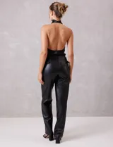 Pantalón de cuero sintético negro, de corte recto y tiro alto. Presenta cintura con hebillas laterales regulables y cierre frontal.