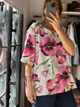 Blusa blanca de corte holgado con diseño estampado de flores grandes en tonos fucsia y hojas verdes, escote redondo y mangas cortas amplias.